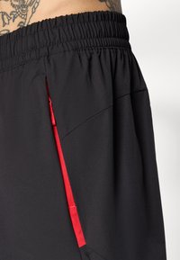 Sorte sportshorts med elastisk talje, der har en rød lynlåslomme og glat, letvægtsstof. Minimalistisk design og funktionel.