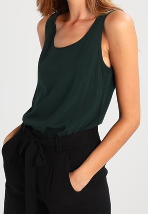 Top senza maniche verde scuro con scollatura a girocollo e texture liscia, abbinato a pantaloni neri a vita alta con dettaglio legato.