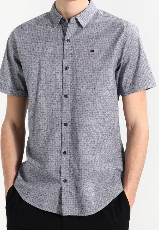 Camicia a maniche corte con bottoni in un motivo geometrico blu e bianco. Presenta un colletto, bottoni scuri e un piccolo logo sul petto.