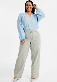 Helles Blau, langärmlige Bluse mit V-Ausschnitt; kombiniert mit hochgeschnittenen, hellgrauen, weit geschnittenen Jeans und beigen Absätzen. Schlichte, lockere Passform.