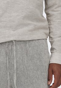 Lichtgrijze longsleeve top gemaakt van textuurstof, gecombineerd met grijs gestreepte broek met een tailleband van trekkoord. Subtiel kleurcontrast opgemerkt.