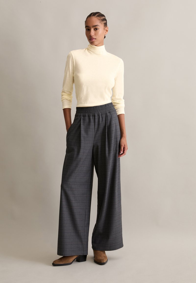 Light yellow mock turtleneck top paired with black and gray check-patterned wide-leg pants. Brown high-heeled shoes complete the outfit.