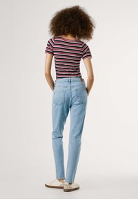 Camiseta ajustada a rayas negras y rojas, jeans de tiro alto de color azul claro y zapatos blancos con elementos decorativos. Diseño simple, estilo casual.