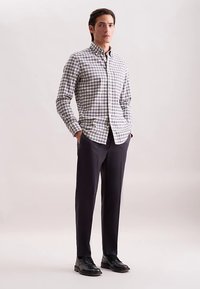 Koszula na guziki w kratę, z odcieniami bieli, granatu i szarości. Dobrana do ciemnych, dopasowanych spodni i czarnych butów.
