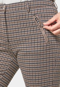 Pantaloni a quadri houndstooth marroni e beige con vestibilità slim, dotati di una tasca con zip sul lato e una texture morbida.