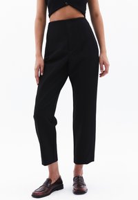 Zwarte high-waisted broek met een rechte snit, voorzien van pinstripe-details. Glad materiaal en zijzakken. Gepaard met bruine loafers.