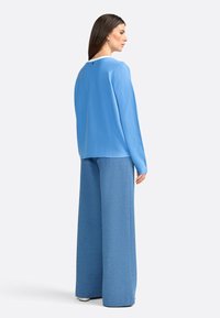 Top blu lungo con maniche, dotato di scollatura rotonda, abbinato a pantaloni blu a vita alta e a gamba larga con texture. Dettaglio di branding discreto sul retro.