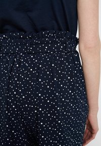 Granatowe spodnie w białe kropki, z falbaną w pasie i plisowanym krojem, wykonane z teksturowanej tkaniny.