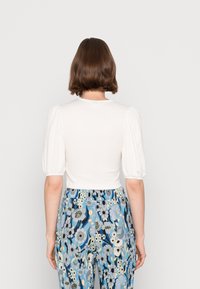 Top bianco aderente con maniche a sbuffo, tessuto texturizzato; abbinato a pantaloni blu a motivo floreale con fiori grandi e dettagli verdi.