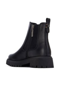 Botas de tobillo negras de cuero con cremallera lateral, suela de goma y puntera redonda. Presentan un lazo en la parte trasera para facilitar el calzado.