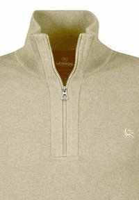 Jasnobeżowy sweter zapinany na zamek z wysokim kołnierzem, prążkowanymi mankietami i małym haftowanym logo po lewej stronie. Miękka faktura, casualowy design.