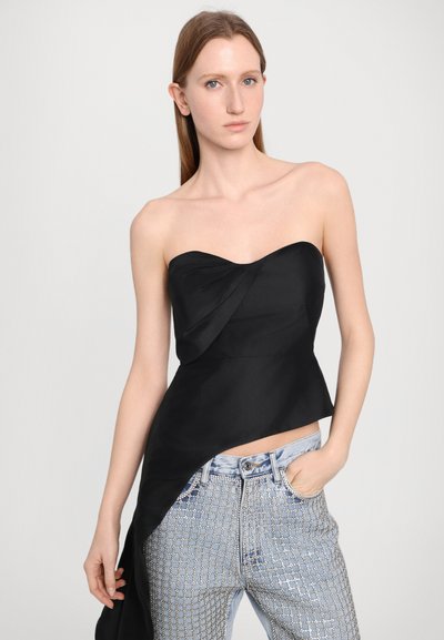 Melnā strapless blūze ar drap�ētu dizainu, kopā ar gaismas zilo džinsu biksēm, kurām ir metalizēti rotājumi un gluda tekstūra.