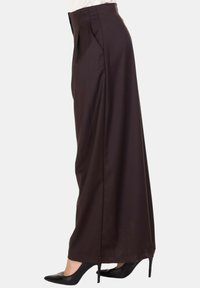 Pantaloni neri a gamba larga abbinati a scarpe con tacco nere, mostrati di lato su uno sfondo semplice.