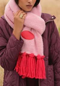 Różowy wełniany szalik z czerwonymi frędzlami, z centralną skórzaną naszywką tłoczoną napisem "Miłość i Róże". Połączony z fioletową pikowaną kurtką.