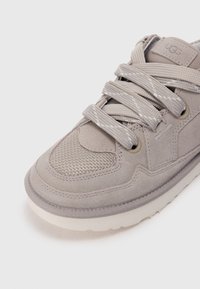 Sneakers grigio scamosciato con dettagli in rete, punta rotonda, suola piatta bianca e lacci grigi con un design testurizzato e un sottile particolare di branding.