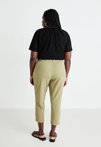 Svart, texturerad t-shirt med kort ärm, matchad med olivgröna byxor som slutar vid anklarna och svarta sandaler. Utsikt bakifrån som visar den lösa passformen och det elastiska midjebandet.