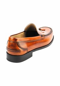 Mocasines de cuero marrón con puntera redonda cosida, borlas decorativas y suela baja de goma negra. Textura suave con un acabado pulido.