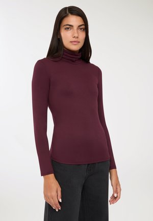 Maglione a collo alto color bordeaux realizzato in tessuto elasticizzato, dalla trama morbida, design aderente con maniche lunghe, abbinato a pantaloni neri a palazzo.