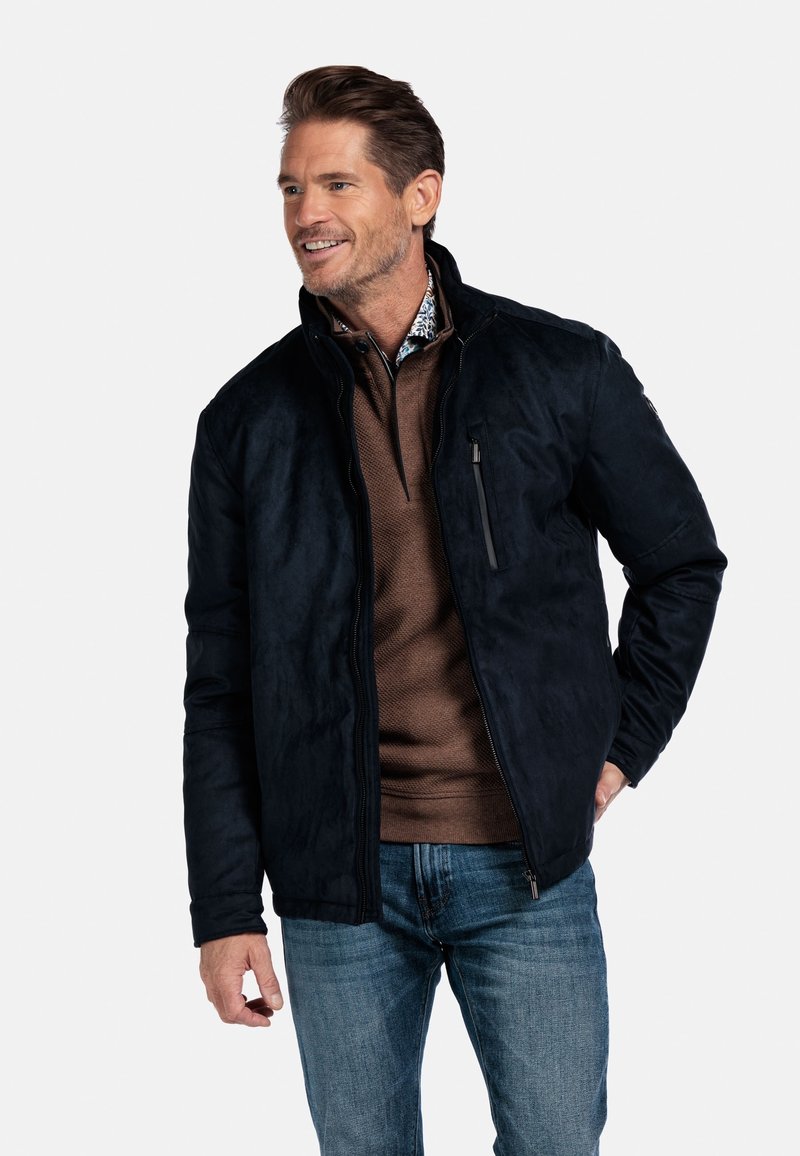 Donker marineblauwe jas met een zachte, suède-achtige textuur, met een ritssluiting aan de voorkant en een borstzak. Geregistreerd over een bruine, gestructureerde shirt.