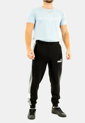 Joggers en negro y gris con cinturilla elástica; presenta un logo y detalles en blanco. Combinados con una camiseta de cuello redondo en azul claro. Zapatillas negras.