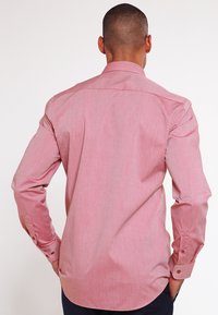 Chemise à manches longues en tissu rose clair avec une finition légèrement texturée, dotée d'un col et de poignets boutonnés, d'un ourlet droit et d'une couture d'empiècement au dos.