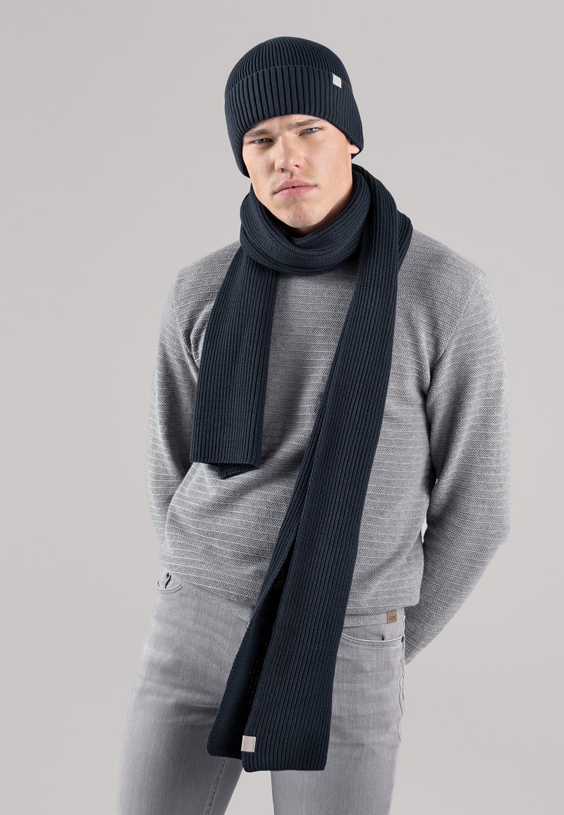 Navy ribbed knit beanie and scarf set, featuring a soft texture and neat edges, paired with a light grey patterned sweater.