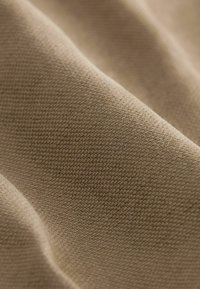 Beige texturerat tyg med en mjuk, vävd utseende, med subtila, enhetliga fibrer och mjuka veck som skapar en jämn yta.