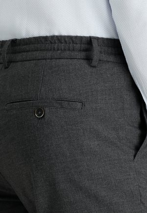 Grijze geweven broek met een achterzak met knoop, elastische tailleband en subtiele structuur, gedragen met een lichtgekleurde shirt.