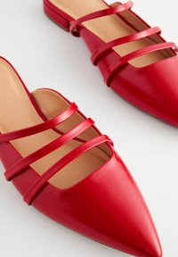 Ballerines en simili cuir rouge avec un bout pointu et quatre brides croisées sur le dessus du pied. Texture lisse avec un profil bas.
