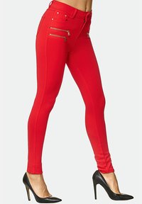 Röda stretchiga skinnybyxor med hög midja, utrustade med två blixtlåsfickor framtill och en slät yta. Matchas med svarta högklackade skor.