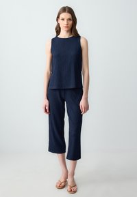 Haut sans manches texturé bleu marine et pantalon court assorti, avec des boutons sur le côté et une coupe décontractée, associé à des sandales tongs beiges.