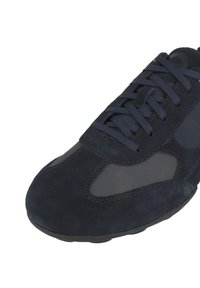 Sneaker in suede blu navy con una texture liscia, caratterizzata da lacci tonali, un design curvo e un pannello laterale semitrasparente. Suola in gomma visibile.