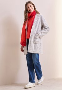 Lys grå fluffy frakke med to forlommer, parret med et rødt ribbet tørklæde, rød top og blå jeans. Hvide sneakers fuldender outfittet.