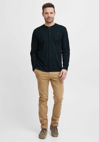 Pikendusega must henley-särgid, millel on nööbid, ja khaki värvi chinos, koos pruuni suède jalanõudega. Lihtne, vabaaja riietus meestele.