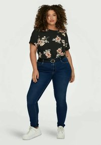 Svart blomstret topp med kort erme, satt sammen med blå skinny jeans og hvite sneakers. Inkluderer et belte med sirkulært spenne.