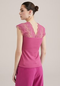 Top aderente rosa con texture a coste e sovrapposizione in pizzo sulle spalle, caratterizzato da uno scollo a V sul retro e maniche a campana.