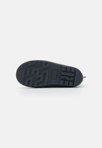 Semelle de sneaker noire avec motif texturé, présentant des rainures angulaires et un logo circulaire. Matériau en caoutchouc flexible, conçu pour l'adhérence et la stabilité.