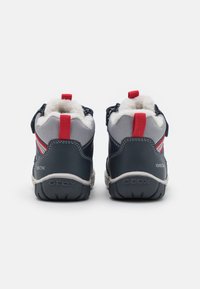 Zapatos altos azul marino y gris con detalles en rojo, con un interior suave, correa de Velcro y suela de caucho texturizada para mejor agarre.