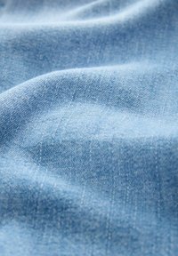 Lichtblauwe denimstof met een zachte textuur, met subtiele variaties in de draadbreedte en een gladde, licht matte afwerking.