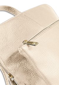 Beige leren rugzak met een textuur en een ritsvak, voorzien van gouden hardware en een gladde afwerking. Ronde hoeken en een minimalistisch ontwerp.