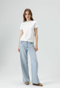 Witte T-shirt met korte mouwen gecombineerd met lichtblauwe wijde jeans en tan schoenen. Effen ontwerp, zachte stof en een ontspannen pasvorm.