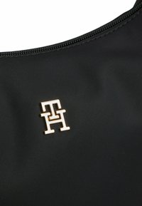 Borsa nera in nylon con superficie texture e logo in tonalità oro. Chiusura con cerniera nella parte superiore. Design semplice e moderno.