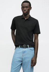 Schwarzes Polohemd mit Kragen, aus Baumwolle, kombiniert mit hellblauen Jeans. Verfügt über ein dezentes Logo und einen Gürtel mit metallischen Akzenten.