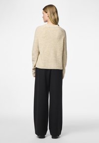 Beige sweater with a textured knit, wide sleeves, and a relaxed fit, paired with loose black pants and simple black footwear.