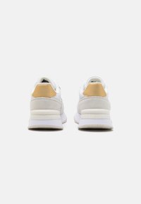 Białe sneakersy z gładką skórzaną i zamszową cholewką, żółtymi akcentami na pięcie oraz białą gumową podeszwą z logo.