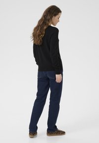 Maglione nero con maniche lunghe, scollatura rotonda e polsini a costine. Abbinato a jeans blu scuro e sneakers marroni con stampa leopardata.