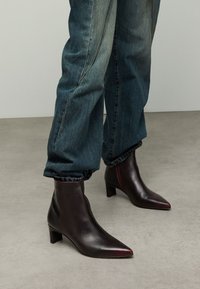 Leren enkellaarsjes met een puntige neus en blokhak, uitgevoerd in een donker bordeauxrode kleur met een gladde textuur. Draagt bij op opgerolde blauwe spijkerbroeken.