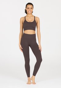 Brauner sportlicher Crop-Top und enganliegende Leggings, beide aus einem glatten, elastischen Stoff. Das Top verfügt über einen breiten Bund, die Leggings haben ein hochgeschnittenes Design.