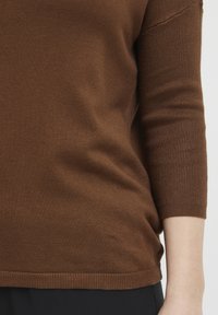 Rjav pleteni pulover s tričetrtinskimi rokavi, ki ima rebrast rob in manšete, gladko teksturo ter oprijet silhueto.