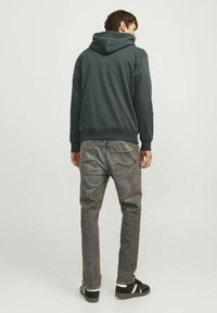 Ciemnoszara hoodie z kapturem na sznurki, w połączeniu z wyblakłymi szarymi dżinsami z tylnymi kieszeniami oraz czarnymi trampkami z białymi paskami.